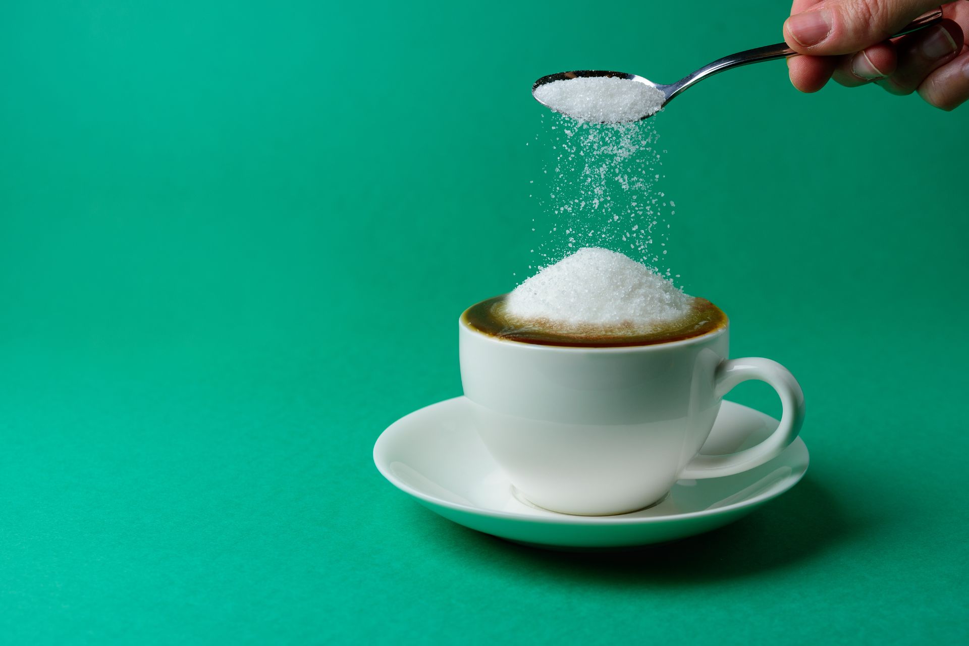 Colher adicionando açúcar em xícara com café
