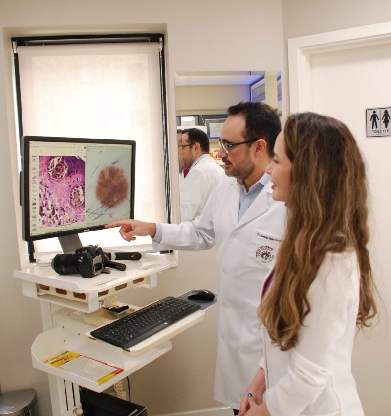 Dermatologistas Dra Laura Bertanha e Dr Leonardo Ávila analisando mancha de pele suspeita em monitor de dermatoscopia na Clínica Pelle Digitale