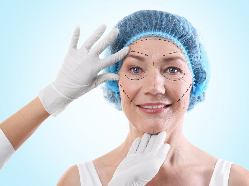 Cirurgião examinando rosto feminino contra fundo azul. Conceito de cirurgia plástica lifting facial